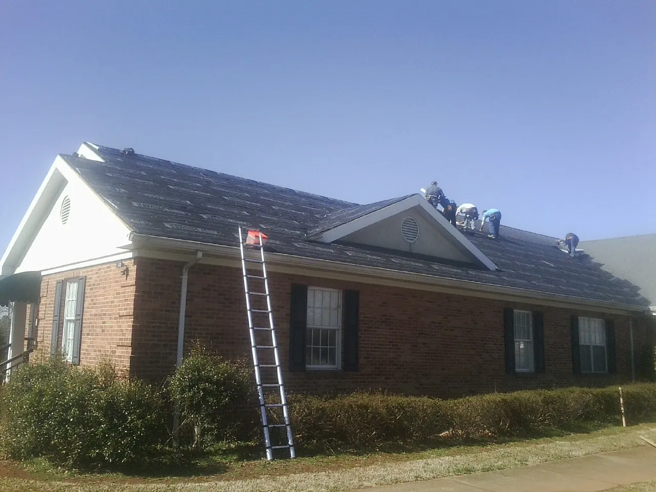 Crew tearing shingles off a brick ranch roof with a ladder set — Metal Roof Repair work by our crew in Orrs Island