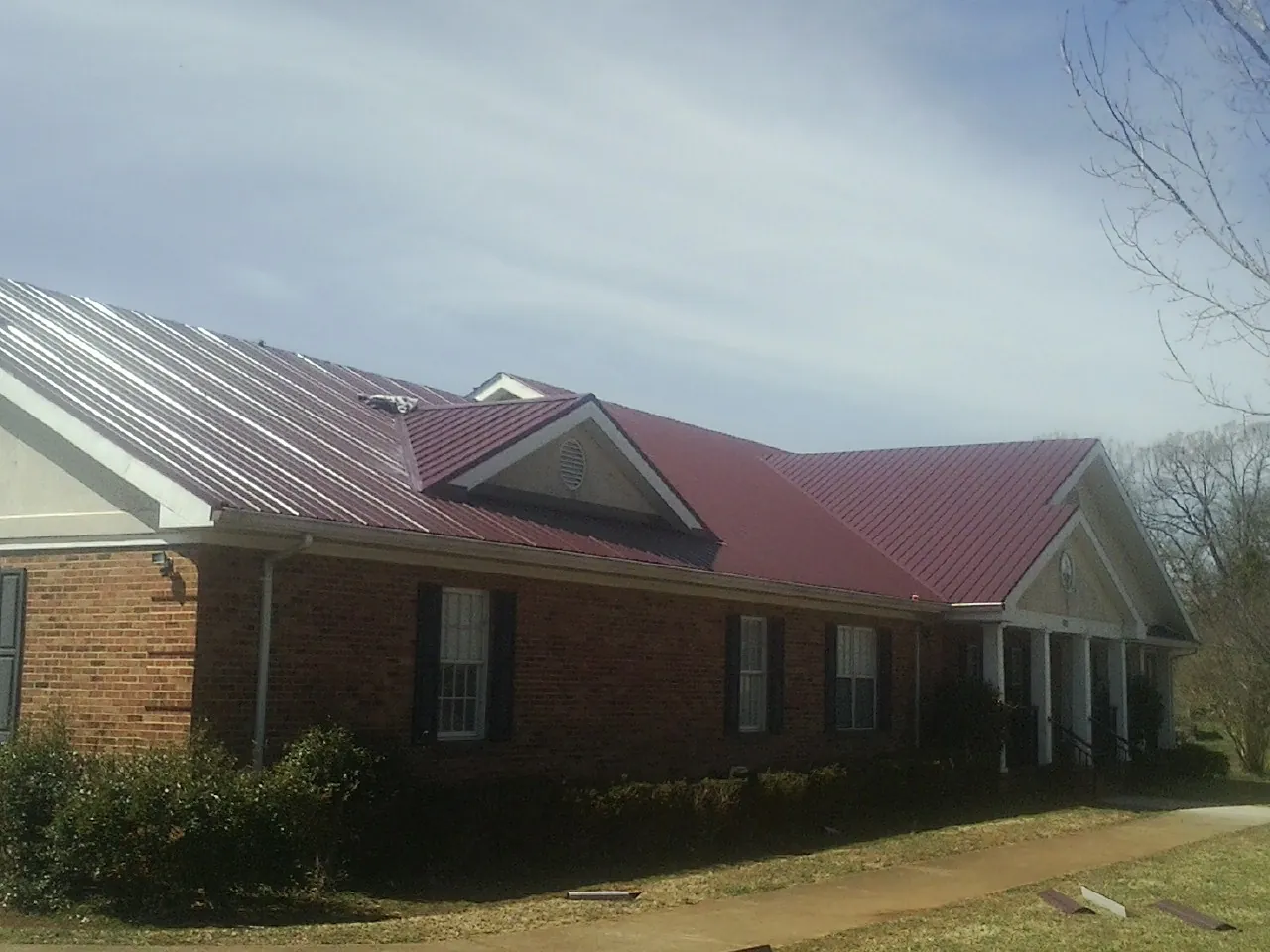 Red metal roof with gabled entries on a long brick building, from a Hail Damage Roof Repair job in Orrs Island