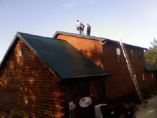 Crew on the ridge of a green metal roof on a two story log home in Orrs Island