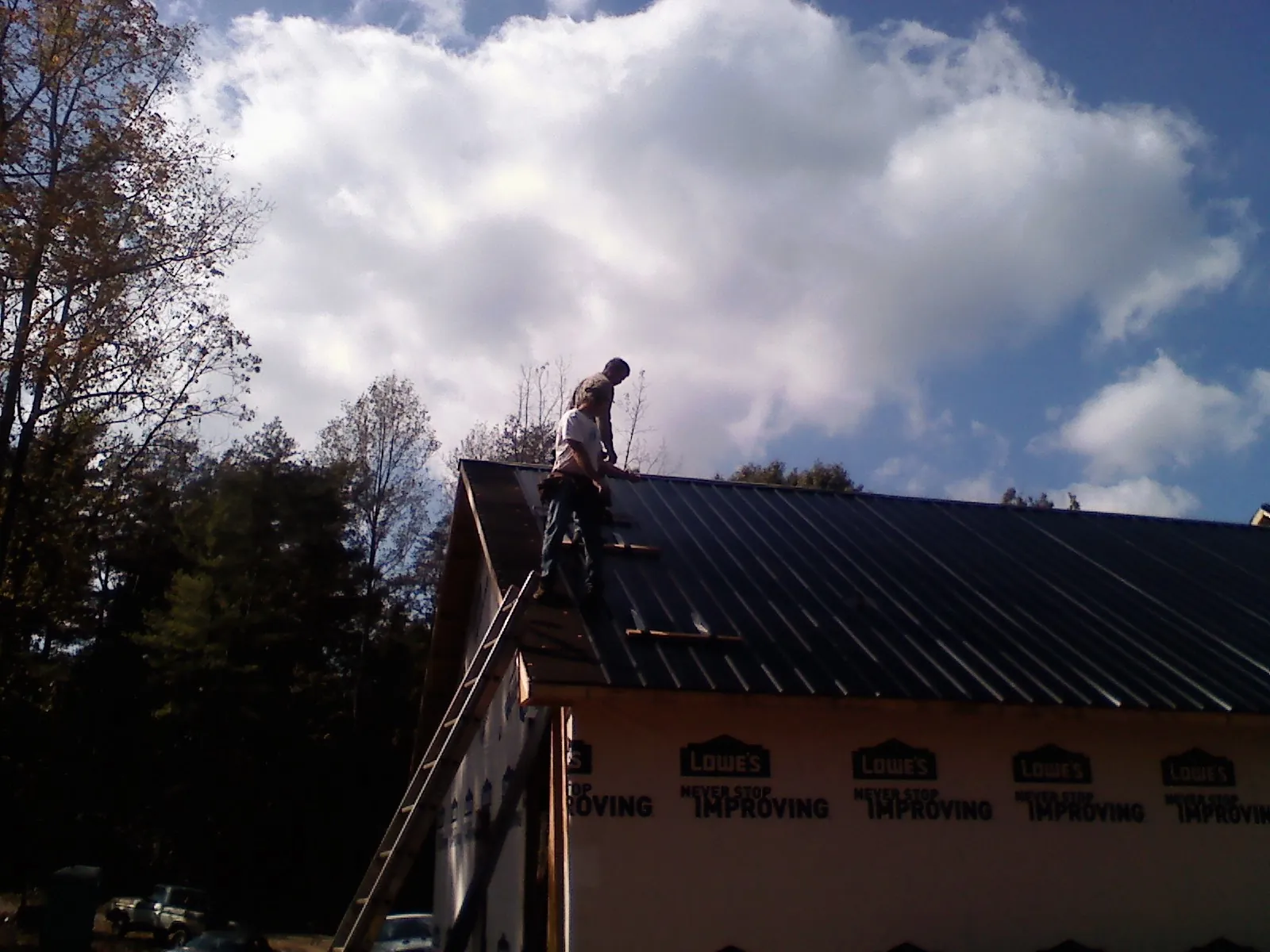 Roofer fastening dark metal panels high against a cloudy sky, from a Roof Inspection job in Orrs Island