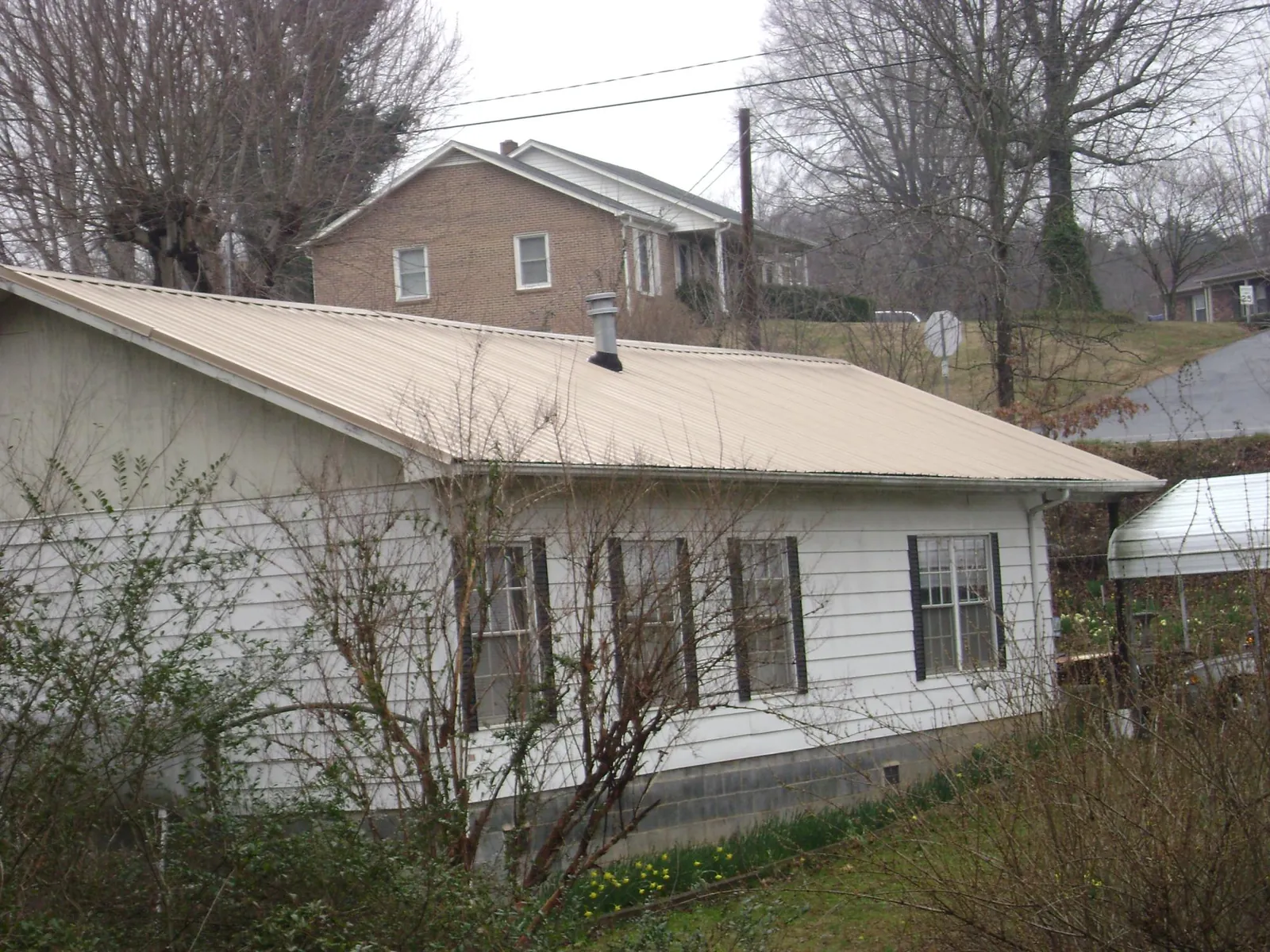 Tan metal roof on a white sided house set into a hillside — Commercial Roofing by Roofing Brothers in Orrs Island